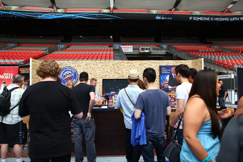 People standing in a sports arena concourse with red seats and a merchandise booth.